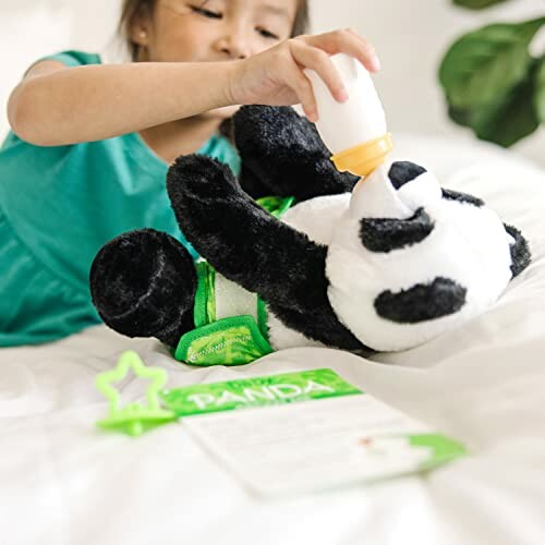 Child feeding a stuffed panda with a bottle on a bed.