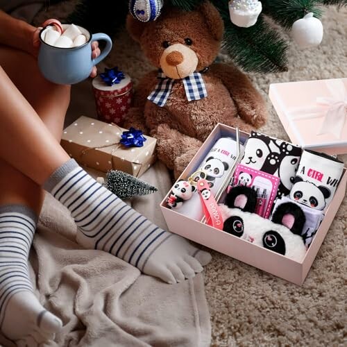 Person with striped socks holding mug, gift box with panda-themed items under Christmas tree.