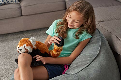 Girl smiling and playing with a red panda plush toy on a couch.