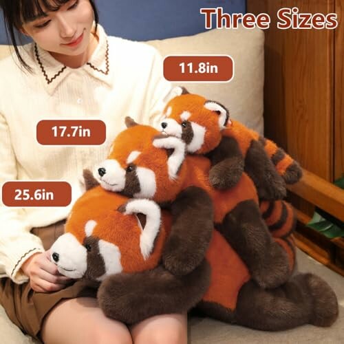 Woman holding three different sizes of red panda plush toys, showing the product's versatility in terms of size.