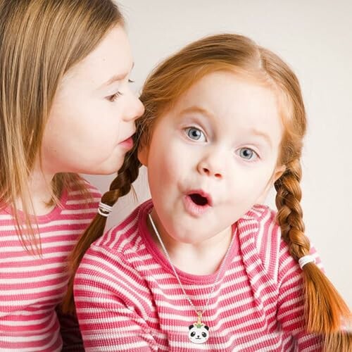 Two young girls in pink striped shirts, one whispering to the other.